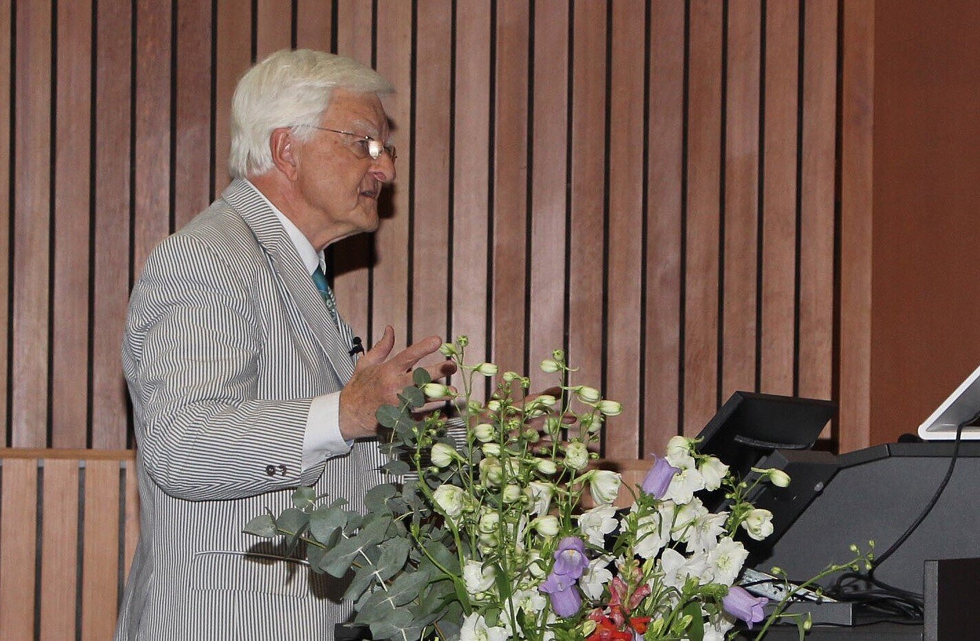 Professor Klaus Viktor Toyka Klaus Viktor Toyka steht am Rednerpult im Hörsaal, vor ihm ein großer bunter Blumenstrauße in einer Bodenvase.