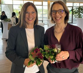 Das Bild zeigt Claudia Sommer und Heike Rittner freudestrahlend nach der Begutachtung, mit Blumen und Sektglas in den Händen. 