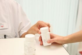 Hi-Nurse überreicht Dose mit Medikamenten 