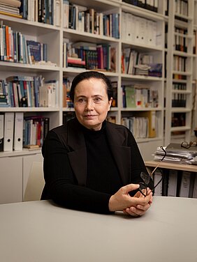 Porträt von Kathleen Wermke am Tisch in ihrem Büro vor dem Bücherregal