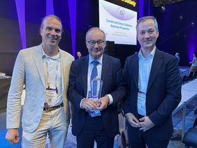 Leo Rasche (links) und Martin Kortüm (rechts) gratulieren beim Kongress Hermann Einsele zum Preis, den er in seinen Händen hält. 