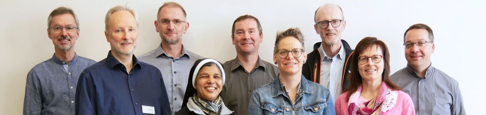 Gruppenfoto: das Team der Seelsorge steht vor einem hellen Hintergrund und lächelt in die Kamera