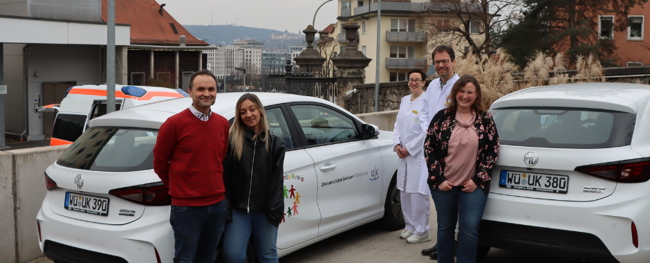 Der Bunte Kreis erhält zwei neue Fahrzeuge für die sozialmedizinische Nachsorge schwerstkranker Kinder und ihren Familien. Auf dem Foto steht das Team des Bunten Kreises und weiteren Klinikleitungen vor den neuen Autos und lächelt dabei.