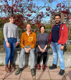 Gruppenbild draußen auf der Terrasse vor dem UKW, Angela Riedel und Leo Rasche sitzen in der Mitte, außen stehen Mara John und Moutez Helal. 