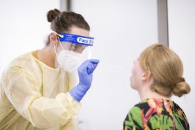 Das  Bild zeigt eine Testsituation am Uniklinikum Würzburg, ein Mitarbeiter entnimmt mit einem Teststäbchen eine Speichelprobe bei einer Probandin. 