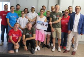 Gruppenbild vom Social Day 2023 in der Küche der Würzburger Berufsfachschule für Diätassistenten: Die Gäste von der Deutschen Bank, angeführt von Dieter Gobernatz (in der Bildmitte zusammen mit Gabriele Nelkenstock vom Verein Hilfe im Kampf gegen Krebs), Prof. Dr. Imad Maatouk vom Uniklinikum Würzburg (rechts), sowie die Schülerin und der Schüler der Diätschule (in Weiß).