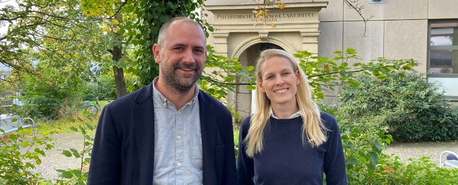 Lorenz Deserno und Vanessa Scholz vor altem Torbogen mit grünen Sträuchern und Bäumen des Zentrums für Psychische Gesundheit am Universitätsklinikum Würzburg