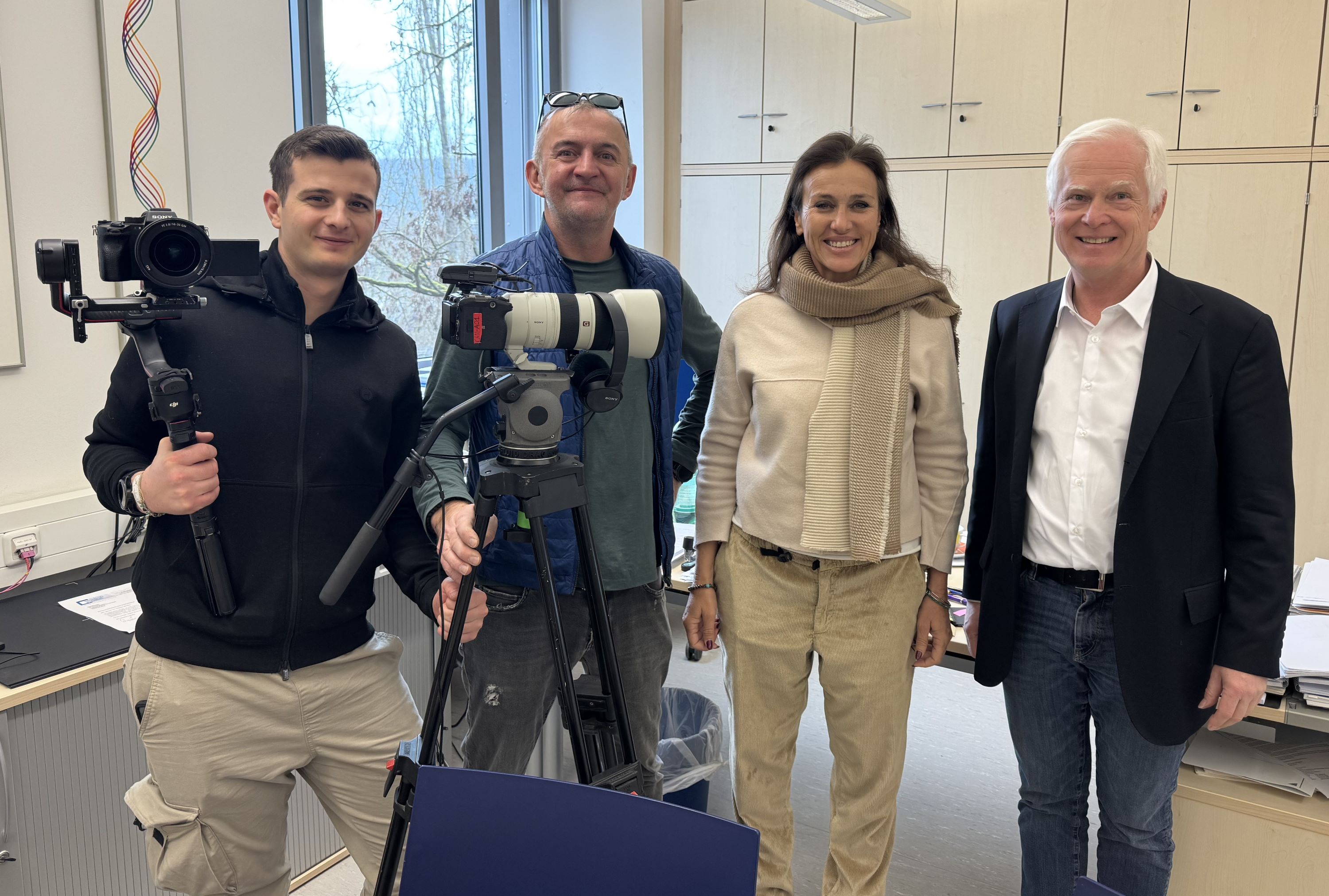 Das Kamerateam posiert mit Michael Sendtner in seinem Büro, Kamera-Equipment steht vor ihnen. 